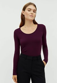 Langärmliges Oberteil aus tiefviolettem Jersey-Stoff mit Rundhalsausschnitt, kombiniert mit hoch taillierten schwarzen Hosen mit Eingrifftaschen.