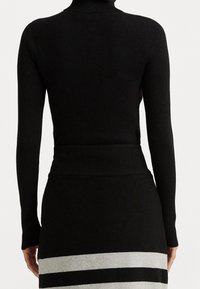 Svart ribbad polotröja med långa ärmar, ihop med en svart kjol med horisontella gråa och vita ränder. Mjuk textur.