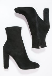 Sorte ruskind ankle boots med spids tå, høj blokhæl, lynlås i siden og syninger for ekstra struktur.