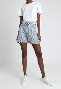 Szorty w paski z wiązanym detalem w pasie, wykonane z lekkiego materiału. Wzór obejmuje pionowe paski w kolorze niebieskim i białym.