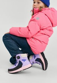 Fioletowe zimowe buty z czarną podeszwą, z solidnym zapięciem i akcentami jasnoszarymi. Noszone przez dziecko w różowej puchowej kurtce i niebieskiej czapce.