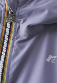 Veste violet clair avec fermeture éclair dotée d'une languette texturée, mise en valeur par des détails rayés vibrants le long de la fermeture.