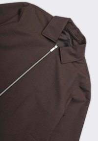 Giacca marrone con una texture liscia, caratterizzata da un colletto a punta e una chiusura frontale con cerniera completa. Il design è minimalista.