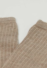 Beżowe dziane skarpetki z delikatną fakturą prążków, z lekko błyszczącą nitką. Górne krawędzie są zawinięte, co dodaje im miękkiego wyglądu.