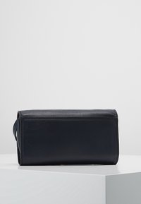 Obdélníková taška tmavě námořnické barvy z hladké kůže s minimalistickým designem. Obsahuje boční uchopovací rukojeť pro snadné nošení.