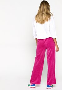 Pantaloni larghi in velluto a coste color fucsia abbinati a una camicia bianca. L'outfit include sneakers colorate con un motivo multicolore.