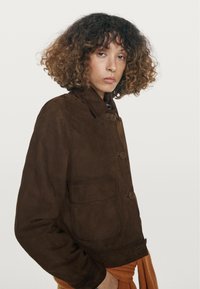 Suède bruine jas met een kraag, knoopsluiting, een zak en een comfortabele pasvorm. De textuur is glad met een zachte afwerking.