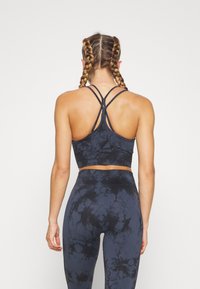 Μπλούζα σπόρ με σχέδιο tie-dye σε μαύρο και γκρι χρώμα, με ράψιμο racerback και λεπτές τιράντες, συνδυασμένη με κολάν tie-dye στο ίδιο σχέδιο. Υφασμάτινη επιφάνεια.