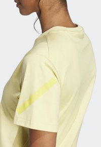 Světle žluté bavlněné tričko s krátkým rukávem. Obsahuje jasně žlutý pruh na levém rukávu a kulatý výstřih.