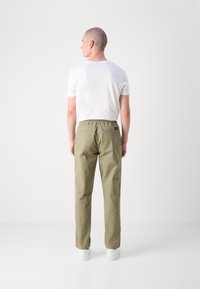 Leichte, elastische Cargo-Hose in Olivgrün mit zwei Gesäßtaschen und einer lässigen Passform, kombiniert mit einem enganliegenden weißen T-Shirt.