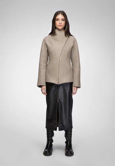 Beige wool jacket with an asymmetrical zip, featuring a high collar. Paired with a black leather maxi skirt and knee-high black boots.