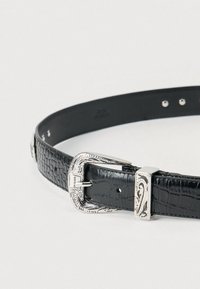 Μαύρη δερμάτινη ζώνη με υφή, διακοσμημένη με ασημένια περίτεχνη αγκράφα και διακοσμητικά στοιχεία. Διαθέτει πολλαπλές τρύπες για ρύθμιση.