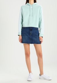 Vaaleansininen lyhyt huppari hupulla ja valkoisilla kolmella raidalla; yhdistetty farkkuminihameeseen, jossa on rispaantunut helma, ja valkoisiin lenkkareihin.