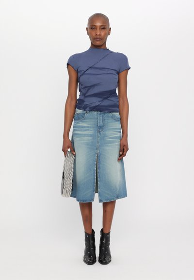 Mørkeblå kortærmet top med snoet design, parret med en lyseblå denimnederdel. Modellen holder en sølvperle-pung og har sorte ankelstøvler på.