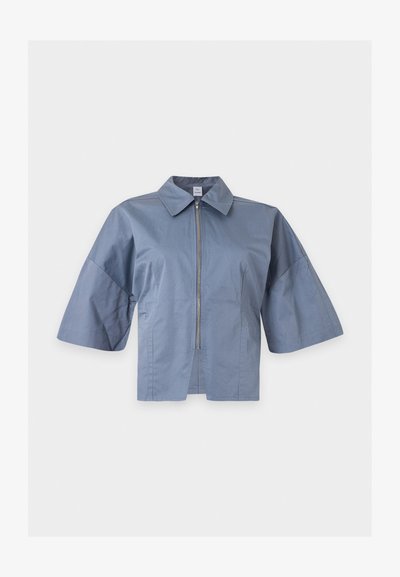 Veste courte bleu clair avec manches larges au niveau des coudes, fermeture éclair devant et col classique de chemise sur fond blanc.