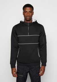 Felpa nera con zip e righe orizzontali bianche. Presenta un alto colletto, tasche laterali e una tasca con zip sulla parte superiore del braccio.