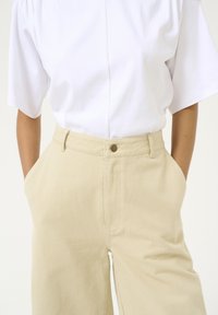 Witte korteglashemd gecombineerd met lichtbeige wijde broek met een knoopdetail aan de voorkant en zijzakken.