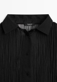 Camicia nera stropicciata con colletto appuntito, chiusura con bottoni e tessuto strutturato. L'etichetta reca la scritta "Massimo Dutti" con un cartellino che indica "Made in China".
