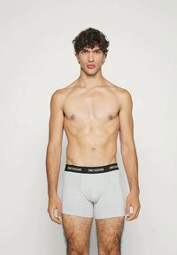 Sivi pamučni bokserici s crnim pojasom na kojem piše "ONLY & SONS." Model je bez majice s neutralnim izrazom lica.