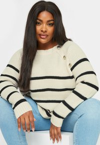 Randig tröja i grädde med svarta horisontella ränder. Tillverkad av stickat material, med knappar på axeln och ribbade ärmslut.