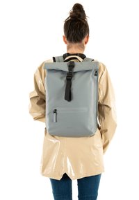 Sac à dos gris à rabat enroulable en mat�ériau imperméable, doté d'une poche avant zippée, de bretelles réglables et d'un design minimaliste.