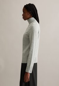 Hellgrauer, langärmeliger Rollkragenpullover mit gerippten Bündchen und Saum, eng anliegendes Design, aus weichem Material, seitliche Ansicht präsentiert.