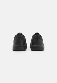 Zapatillas negras con un acabado texturizado, punta redondeada y suelas de goma resistentes. Presenta una lengüeta en el talón y un discreto acento de marca.