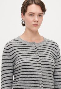 Gråstripet cardigan med rund hals, knappelukking og teksturert stoff. Svart horisontale striper står i kontrast til den grå bakgrunnen.