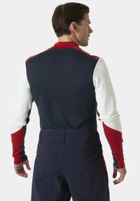 Marineblauwe pullover met rode en witte accenten, voorzien van lange mouwen en een slim fit ontwerp; de achterkant toont een gladde textuur en kleurblokken.