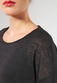 Schwarzer leichter Pullover mit weitem Ausschnitt, der eine lockere Passform und transparente Textur aufweist und ein dezentes Webmuster zeigt.