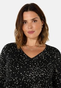 Black dress featuring a V-neck, long sleeves, and a gathered waist. Decorated with small cream-colored heart-shaped prints across the fabric.