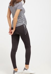 Top de rayas ajustado con costuras laterales fruncidas, combinado con leggings negros lisos y zapatillas blancas con detalles grises.