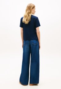 Μπλε βαμβακερό μπλουζάκι με κοντά μανίκια, συνδυασμένο με φαρδιά, ψηλόμεση μπλε τζιν παντελόνια, που διαθέτουν πίσω τσέπες και κλασική κοπή.