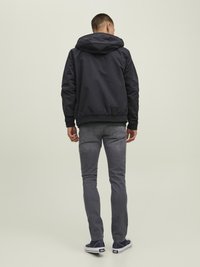 Granatowa kurtka z kapturem z elastycznymi mankietami, noszona na zielonym swetrze, w komplecie z szarymi jeansami slim fit i granatowymi sneakersami. Widok z tyłu.