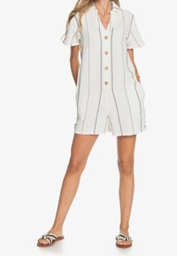 Combinaison courte rayée en blanc et marine, avec un col en V, des manches courtes, une fermeture à boutons et des poches latérales. Tissu doux et coupe décontractée.