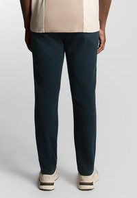 Marineblaue Hosen mit schmalem Schnitt, aus weichem, elastischem Stoff, kombiniert mit hellbeigen Schuhen mit weißen und braunen Akzenten.