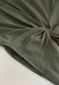 Olivengrüner, sanfter Strickstoff mit einem verdrehten Knoten in der Mitte, ausgestattet mit glatter Textur und genähten Kanten.