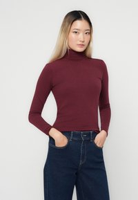 Bordo pitkähihaine turtleneck-paita, jossa on istuva malli. Yhdistetty korkeavyötäröisiin sinisiin farkkuihin. Silkkinen pinta ja joustava kangas.