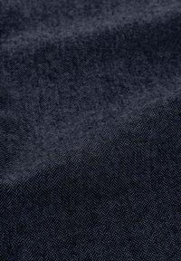 Tessuto blu scuro con un sottile motivo a spina di pesce, texture liscia e una piega diagonale che indica flessibilità e qualità di drappeggio.