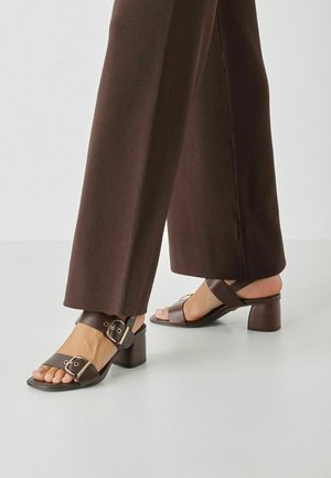 Sandales à talons marron avec larges brides ornées d'une grande boucle, tige texturée et talon moyen épais pour plus de stabilité.