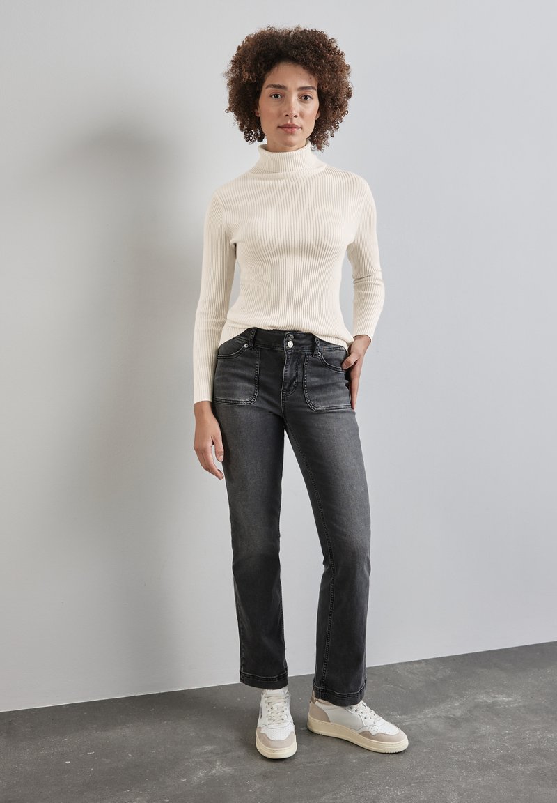 Weißer gerippter Rollkragenpullover, graue Denim-Jeans mit Taschen und helle Sneakers. Einfaches Design, figurnah geschnitten und strukturiertes Material.