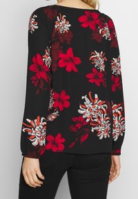 Blusa negra de manga larga con un patrón floral en rojo, blanco y naranja. Tejido suave con un corte relajado y escote redondo.
