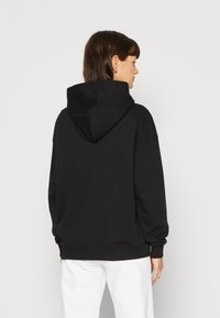 Felpa nera con cappuccio, dal fit rilassato, maniche ampie e polsini a costine. Texture morbida, design semplice, senza grafiche o motivi visibili.
