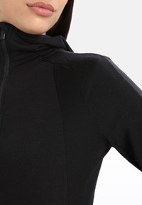 Giacca atletica nera con zip, caratterizzata da un design elegante e aderente con pannelli testurizzati sulle spalle e un tessuto morbido al tatto.