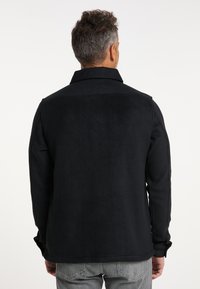 Jachetă din fleece neagră cu un design cu guler. Prezintă o textură netedă, mâneci lungi și o tivă dreaptă. Vederea din spate nu arată accente notabile.