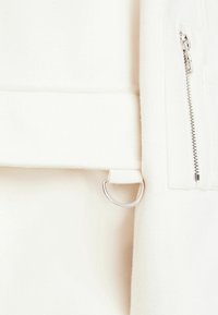 Biała tkanina polarowa z metalowym pierścieniem i kieszenią na zamek błyskawiczny, o gładkiej teksturze i minimalistycznych detalach designu.