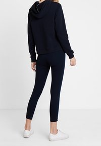 Marineblauwe hoodie met een cropped ontwerp, voorzien van een trekkoordcapuchon en geribbelde manchetten, gecombineerd met hoog getailleerde marineblauwe leggings en witte sneakers.
