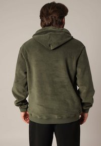 Olijfgroene hoodie gemaakt van zachte stof, met een ontspannen pasvorm, ribbels aan de mouwen en onderkant. De achterzijde toont minimale ontwerpelementen.