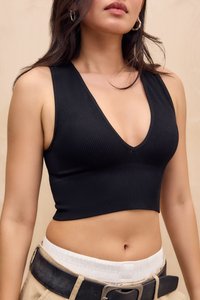 Frau, die ein schwarzes, geripptes, ärmelloses Crop-Top und beige Hosen mit einem schwarzen Gürtel trägt, von den Schultern bis zur Taille vor einem einfarbigen Hintergrund gezeigt.