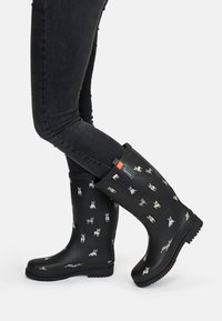 Black rubber rain boots featuring a dog pattern in various colors, textured sole, and a solid black upper with a bright orange accent.